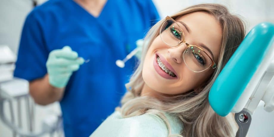 woman with braces wearing glasses, in dental exam chair, smiling