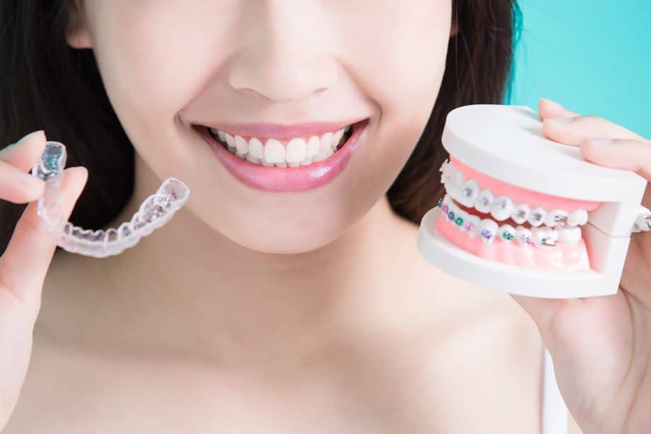 woman holding an Invisalign tray and a teeth model with braces