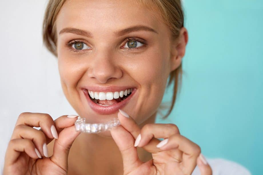 smiling woman holds an Invisalign clear aligner tray