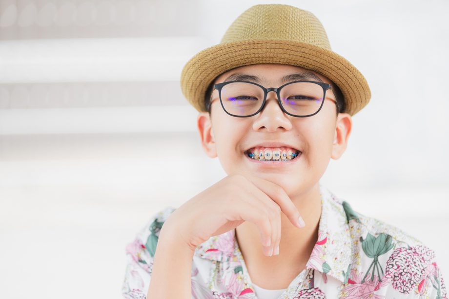 boy in hat and glasses smiles to display his braces